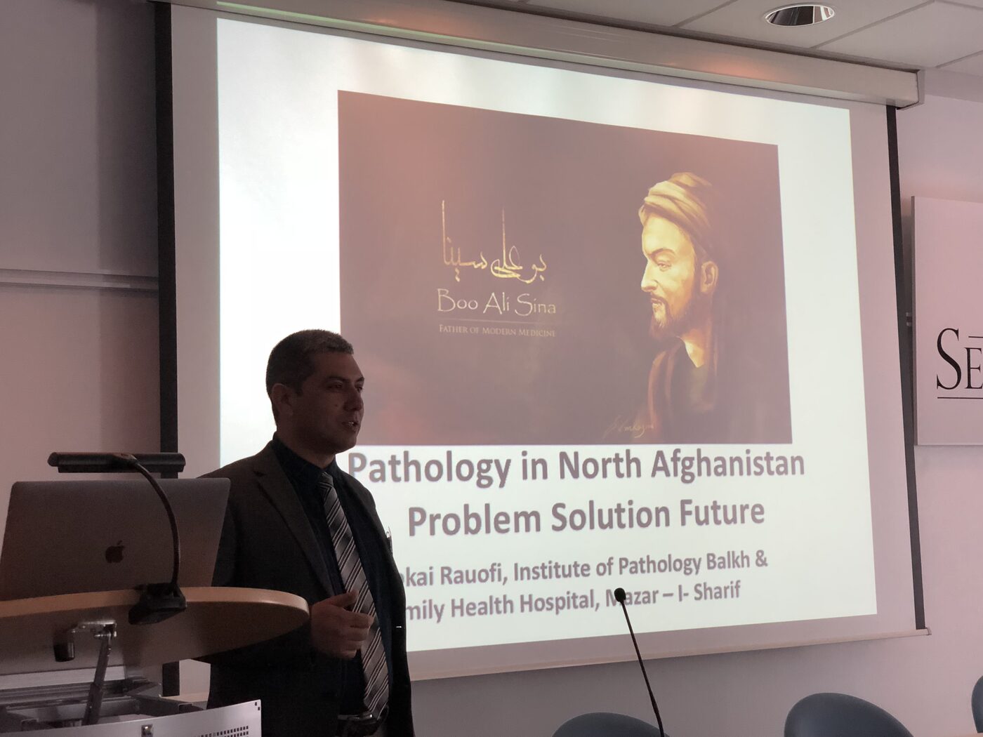 Dr Rauofi of the Institute of Pathology Balkh and the Family Health Hospital, Mazar-i-Sharif, presents on pathology in north Afghanistan, the title slide behind him carrying a portrait of Boo Ali Sina.