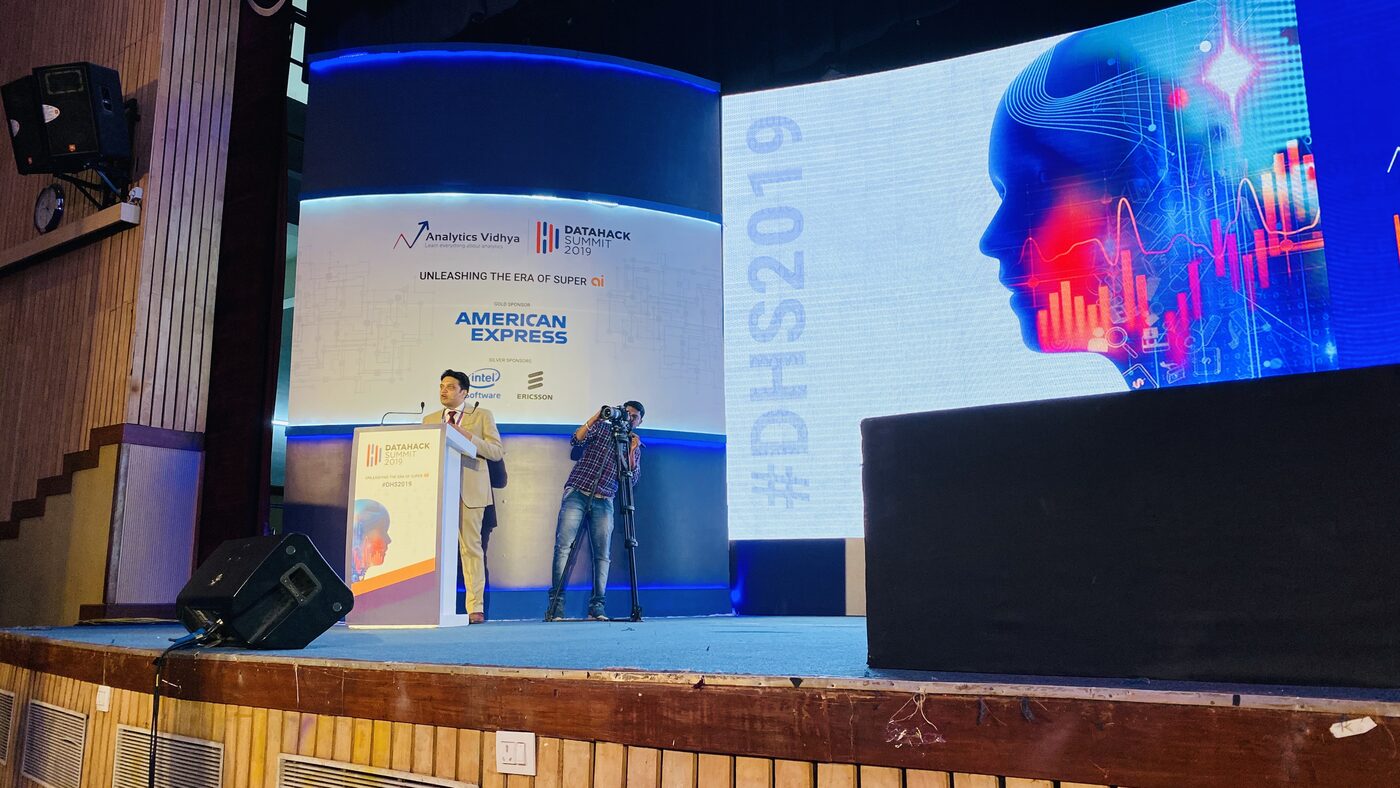 The DataHack Summit 2019 main stage, with the speaking podium at left and a large screen carrying the #DHS2019 artwork and the sponsor panel.
