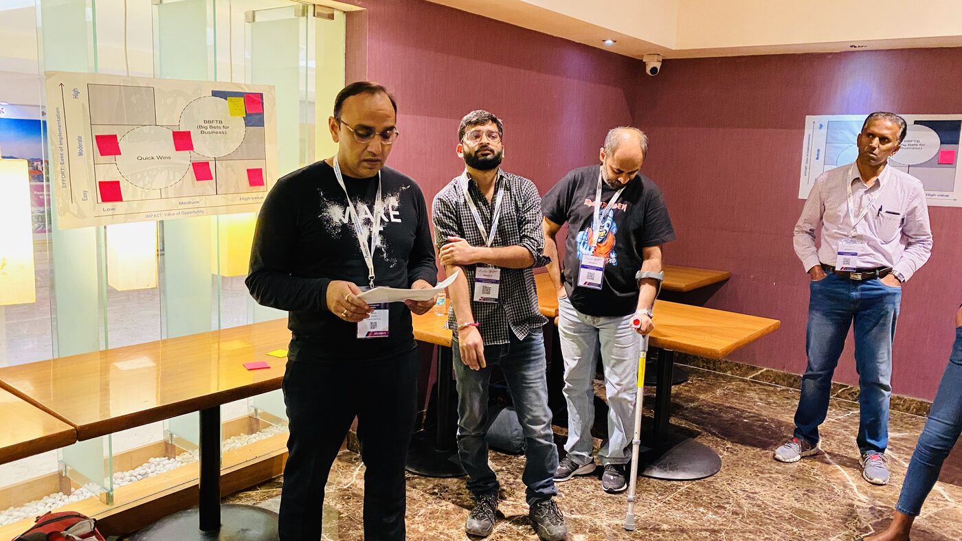 Workshop participants standing at a wall canvas that plots initiatives by effort against value of opportunity, with sticky notes placed in the Quick Wins and Big Bets for Business zones.