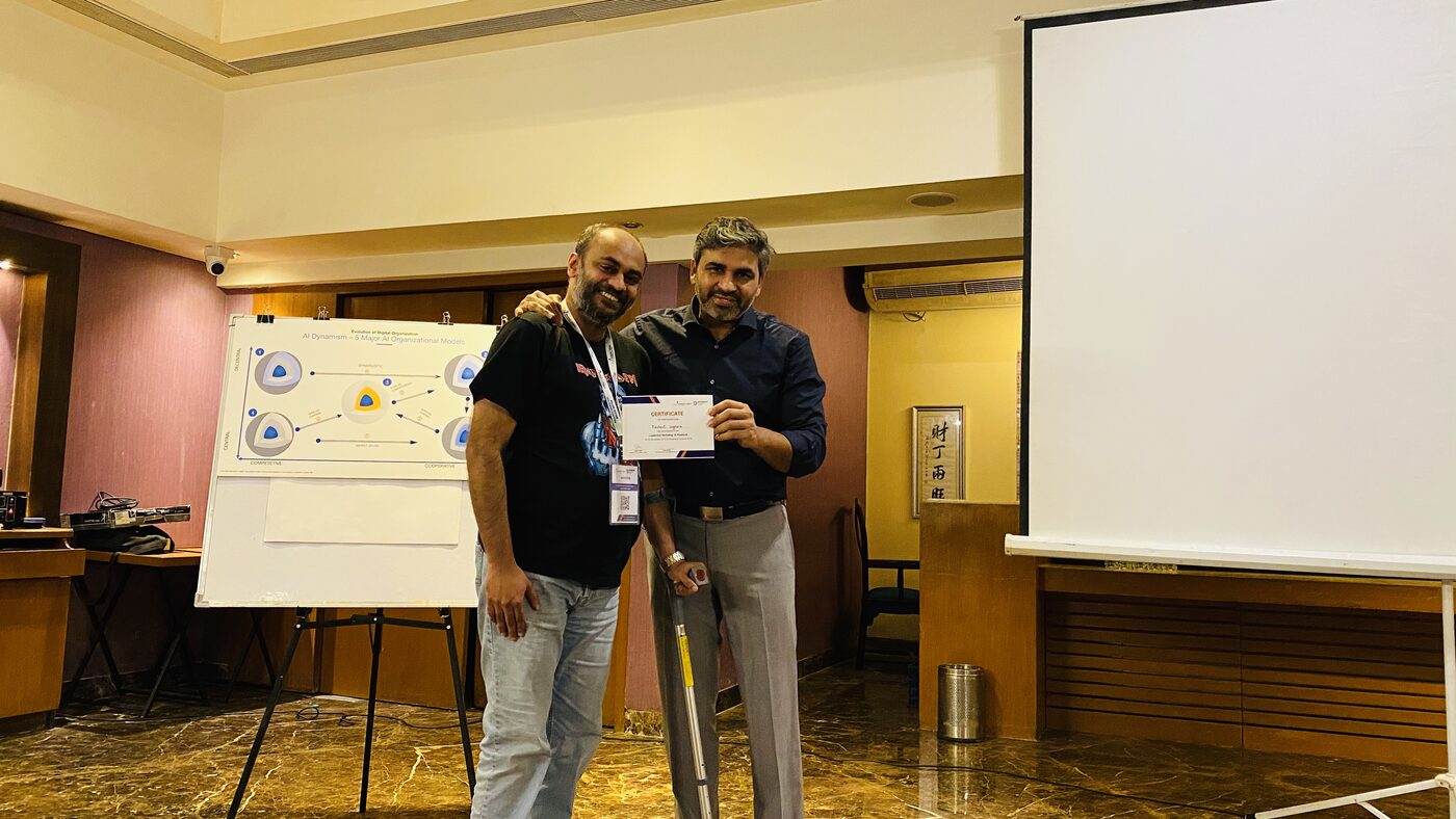 A participant receiving a certificate of participation beside a flip chart drawing of the five AI organisational models.