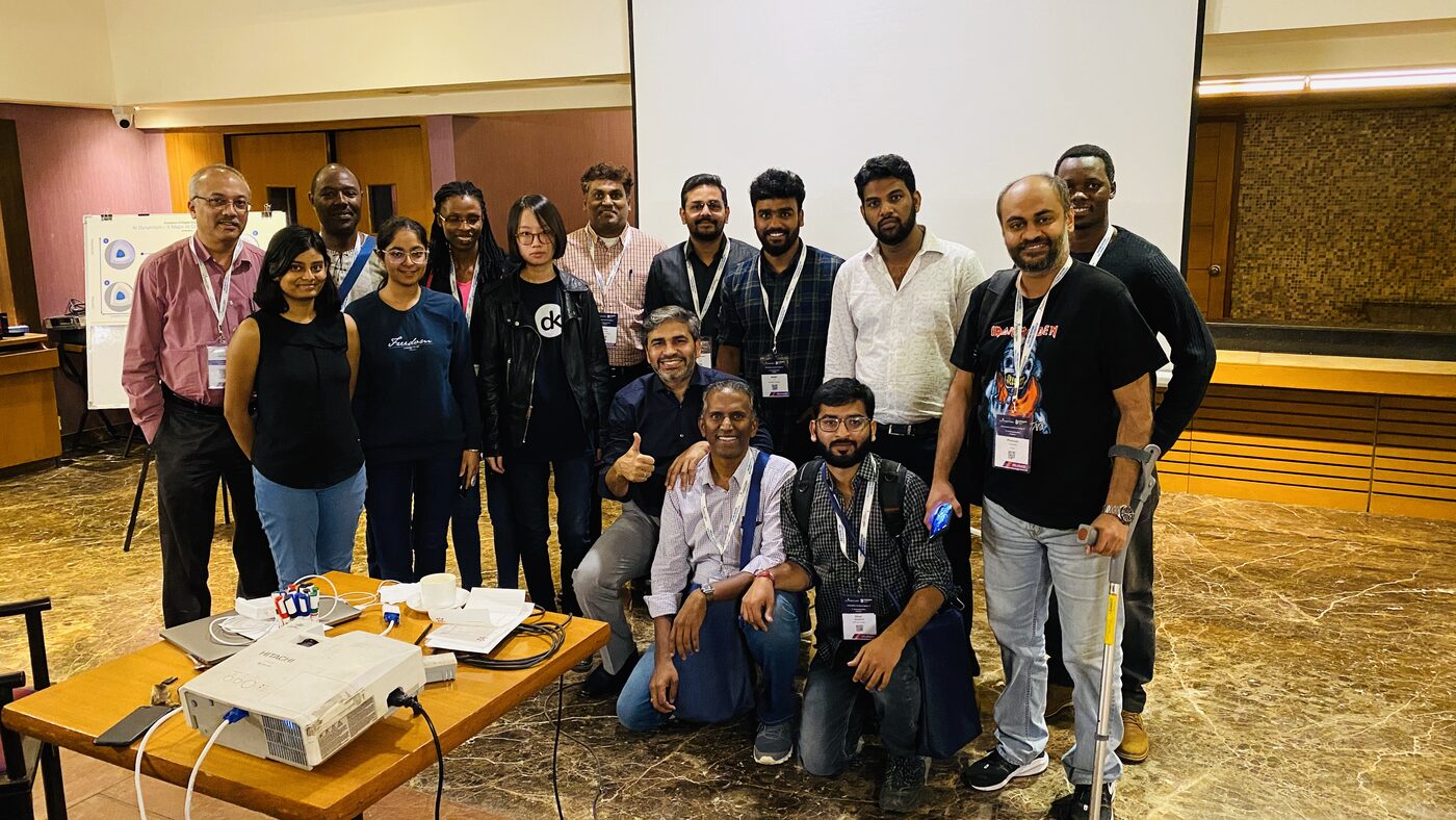 The AI Playbook cohort together at the end of the workshop day, standing behind the projector table in the function room.