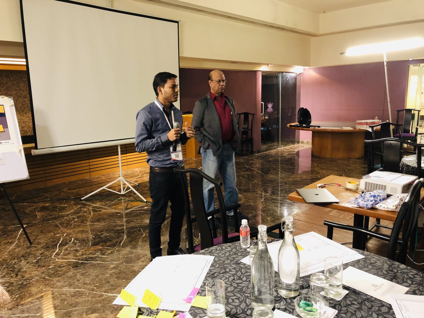 A participant speaks into a handheld microphone beside the projection screen while a second delegate waits to take over.