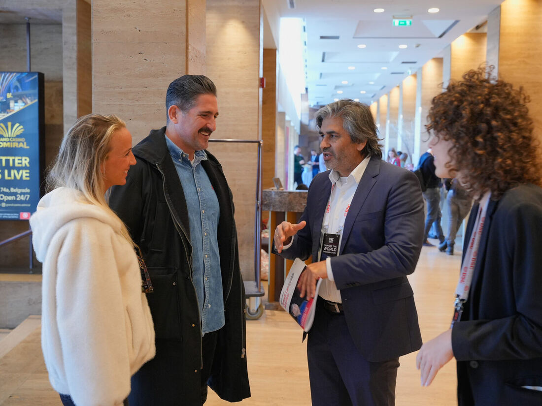 Tarry Singh talks with three delegates in the hotel foyer, holding the conference magazine