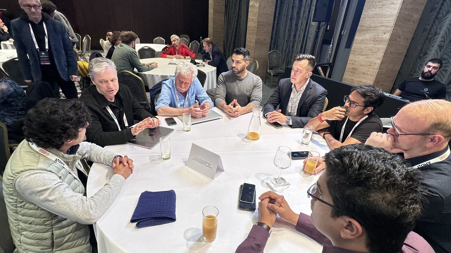 Ten people around a round table in discussion, AMD and DSC lanyards, a printed question card standing in the middle of the cloth.