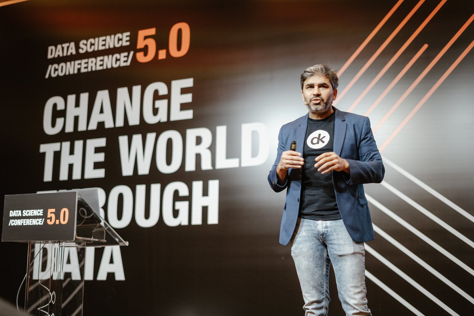 Tarry Singh on the Data Science Conference main stage in Belgrade, handheld microphone, in front of the full-height backdrop reading DATA SCIENCE CONFERENCE 5.0, CHANGE THE WORLD THROUGH DATA.