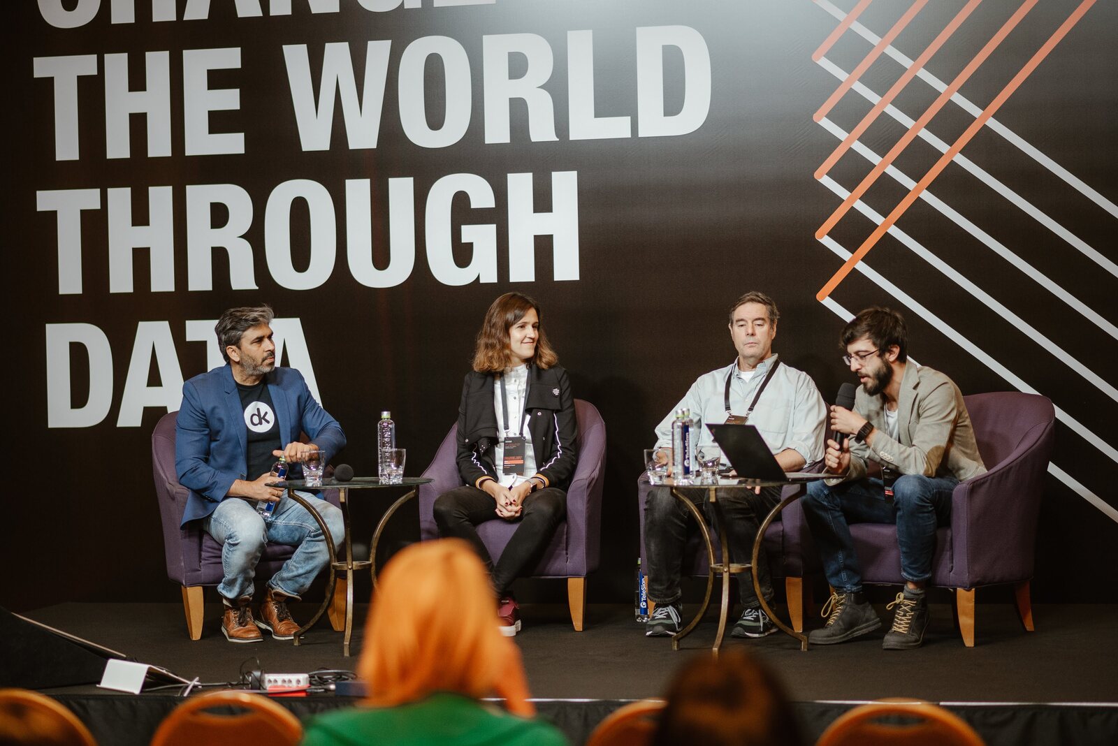 A four-person panel in armchairs on the main stage, the conference backdrop behind them and the audience in the foreground.