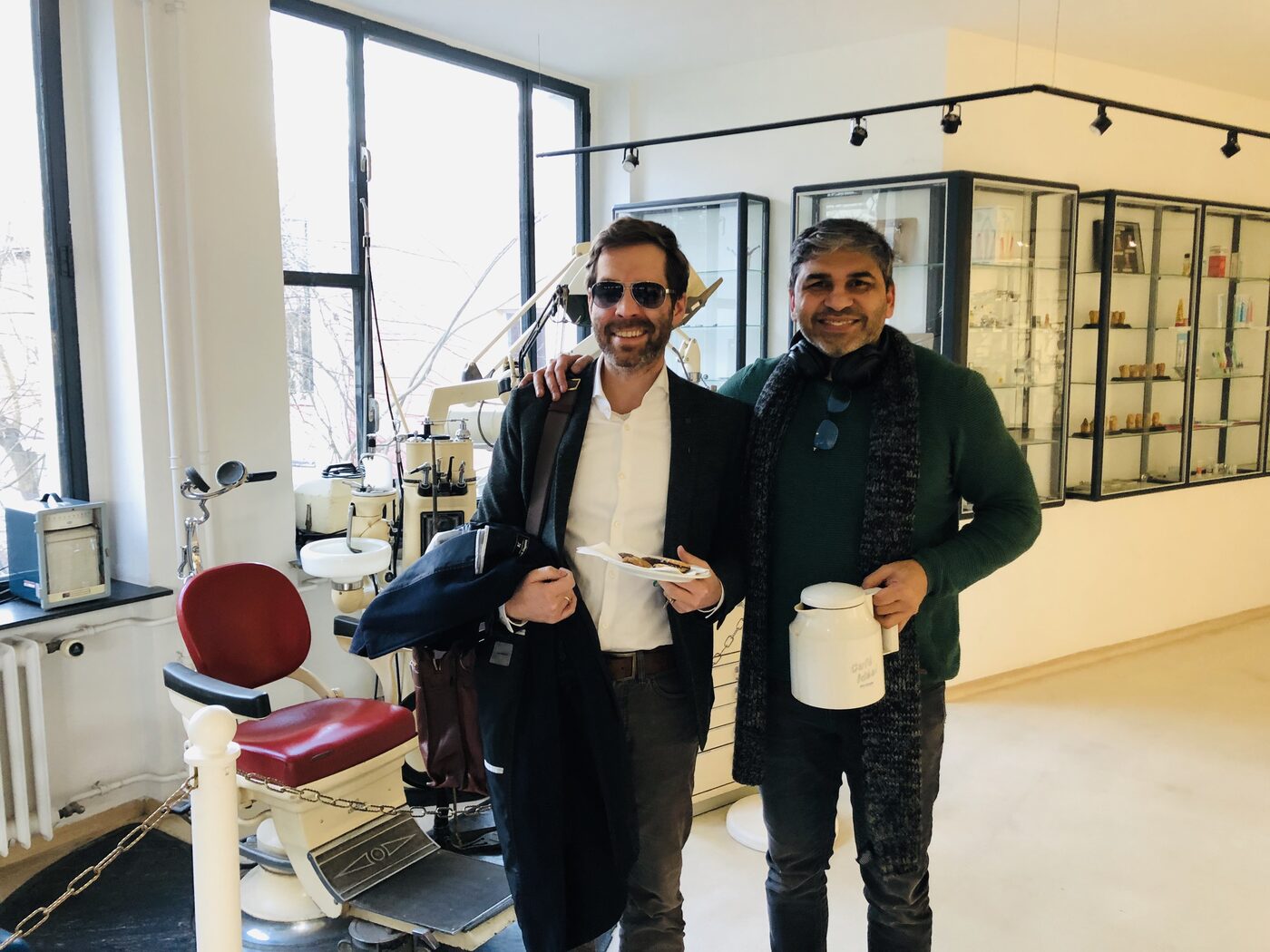 Tarry Singh stands with an unnamed colleague beside a historic dental treatment chair, in a room lined with glass display cabinets, south west Berlin, afternoon of 12 February 2019.