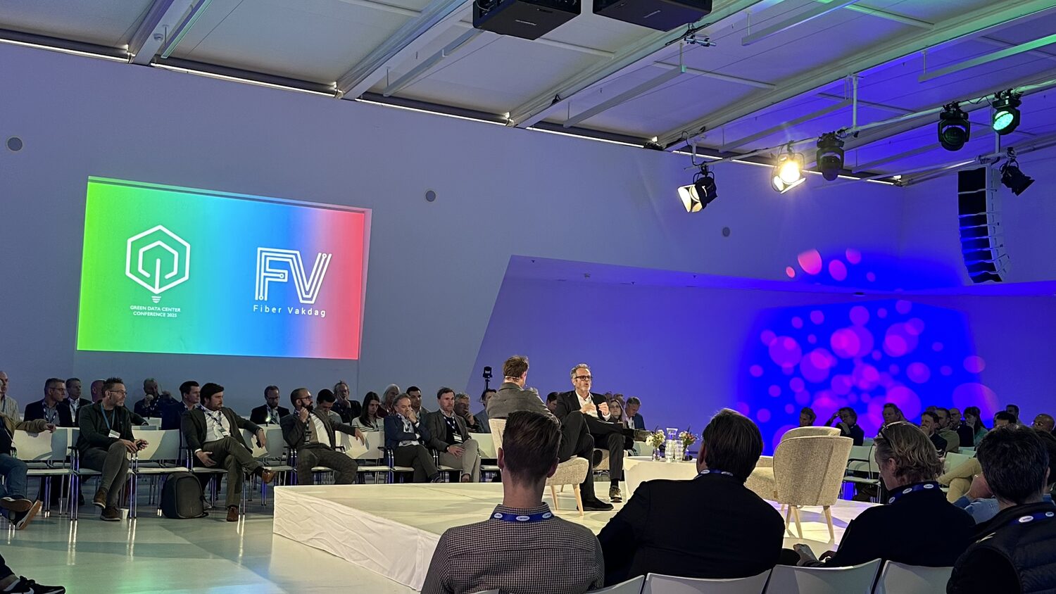 Fireside chat in progress on the plenary stage, the Green Data Center Conference 2025 and Fiber Vakdag logos filling the screen to the left.