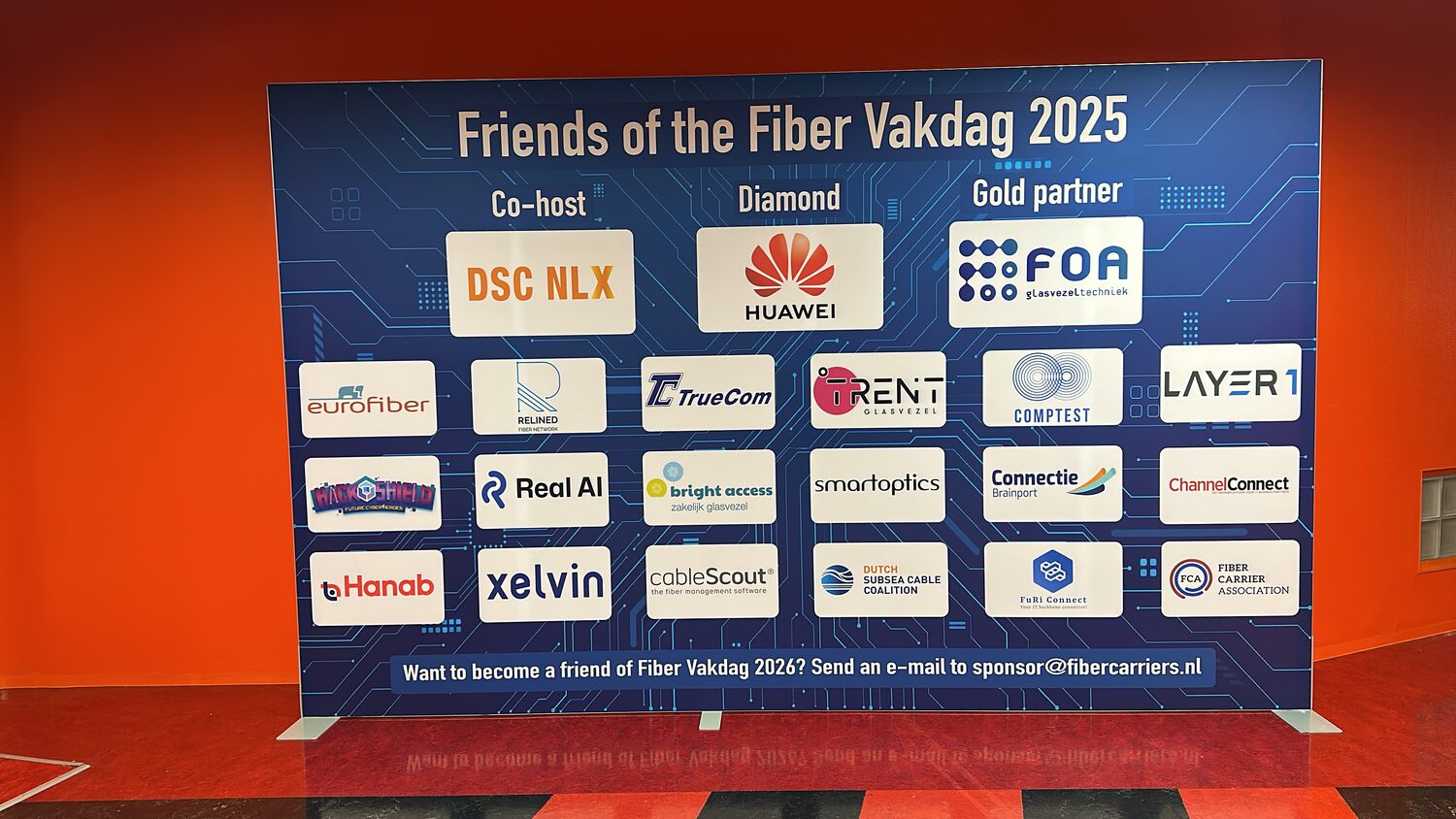 The Friends of the Fiber Vakdag 2025 sponsor wall against an orange partition, DSC NLX listed as co-host, Huawei as diamond partner and FOA as gold partner.