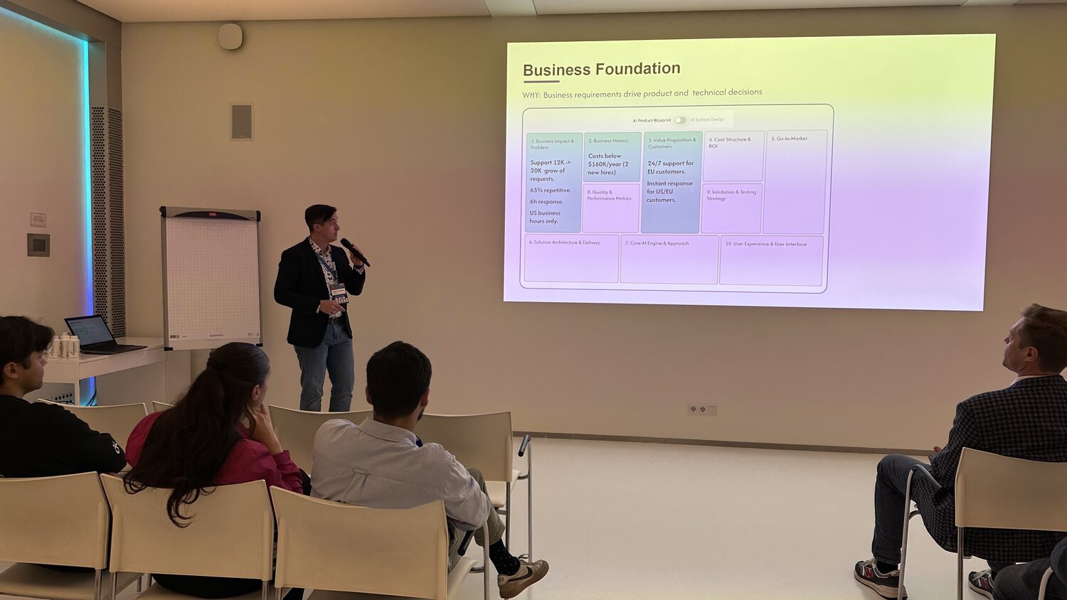 A side room at Spark, a speaker with a microphone in front of a projected AI product canvas, a small group of delegates watching from white chairs.