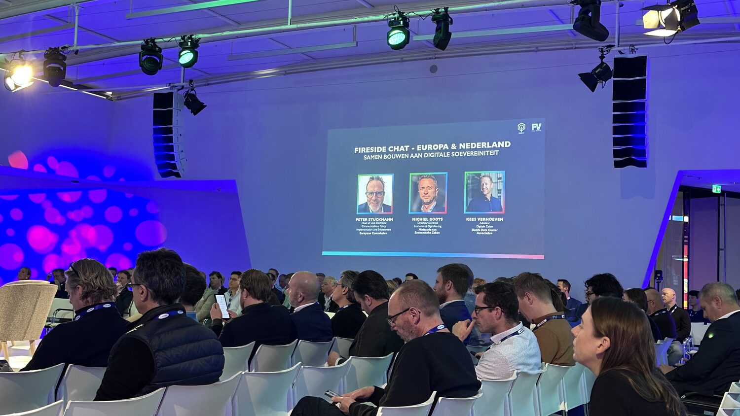 Delegates seated in the plenary, the opening panel card on screen naming Peter Stuckmann, Michiel Boots and Kees Verhoeven.