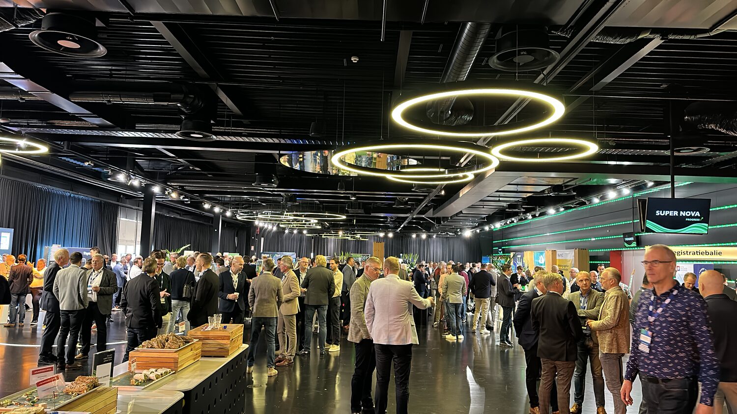 The exhibition hall before the sessions, ring lights overhead, delegates gathered near the registration desk.