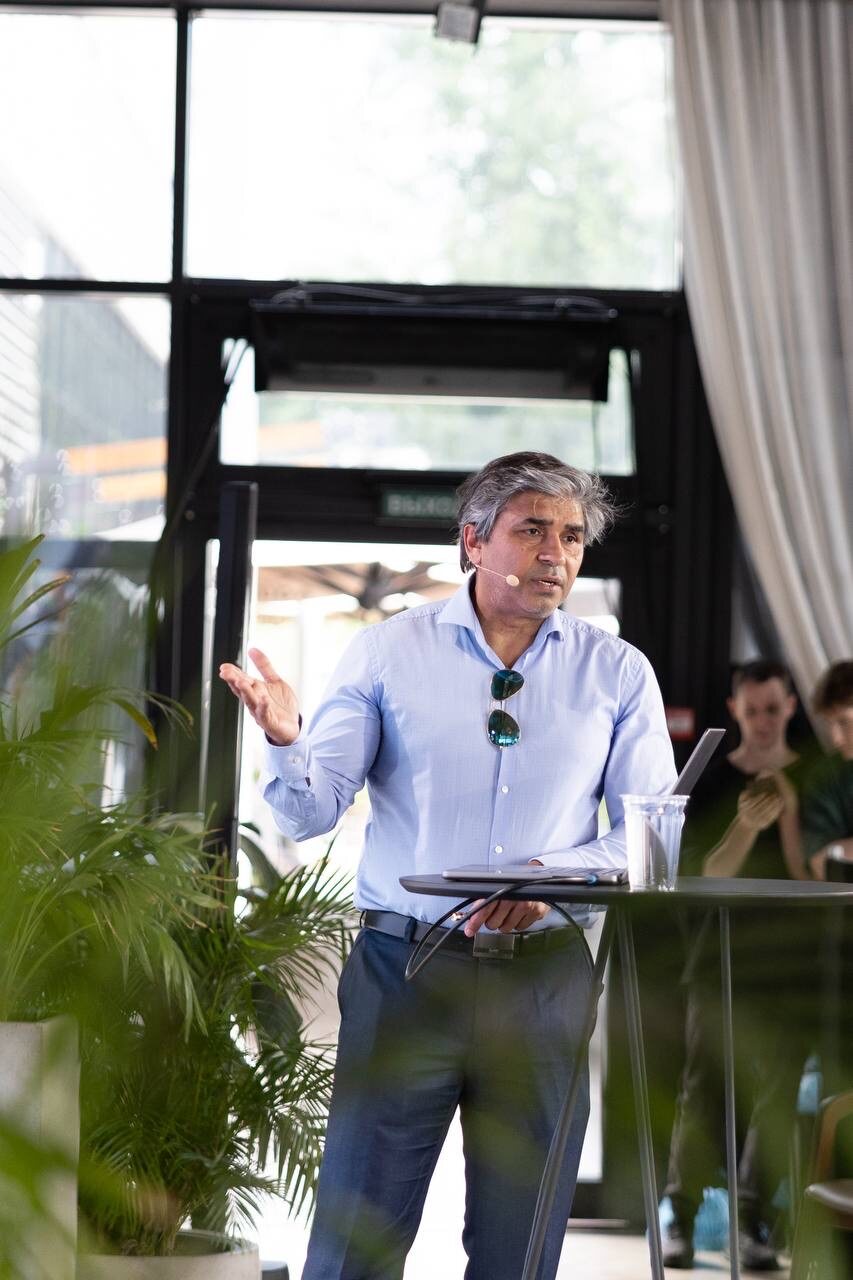 Mid-argument at the lectern, lapel microphone on, working the room rather than the slides.