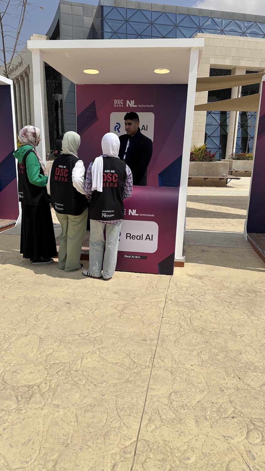 Volunteers in ASK ME DSC MENA vests at the Real AI B.V. stand on the Egypt University of Informatics campus.