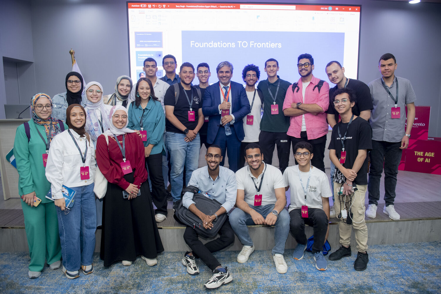 Tarry Singh with a cohort of about twenty students and staff in front of the Foundations TO Frontiers title slide in the university auditorium.