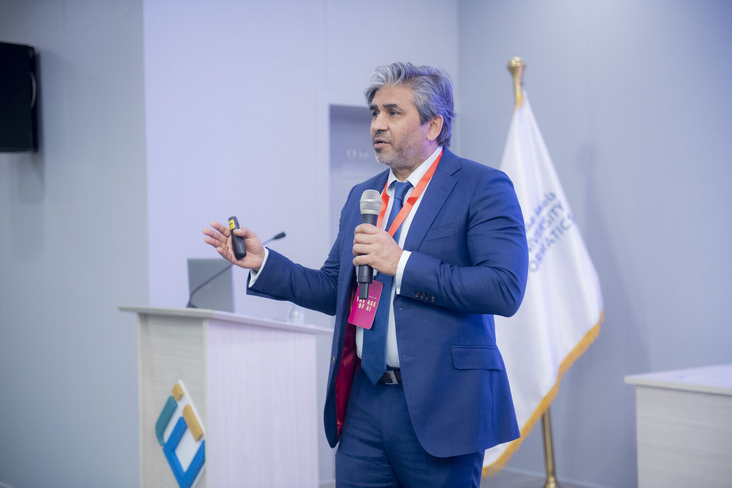 Tarry Singh at the lectern with a microphone and a presenter clicker, the Egypt University of Informatics flag behind him.