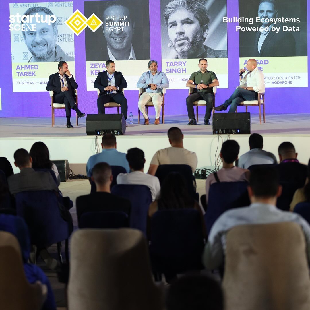 Wide shot of the five-man data panel on stage at RiseUp Summit, seated audience filling the foreground