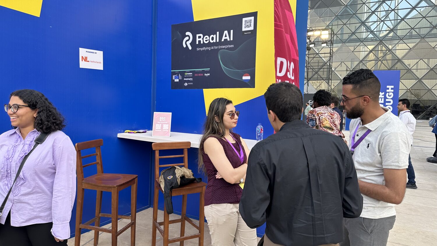 Real AI board reading Simplifying AI for Enterprises on the DSC MENA stand, with a Powered by NL Netherlands plate and visitors talking in front of it
