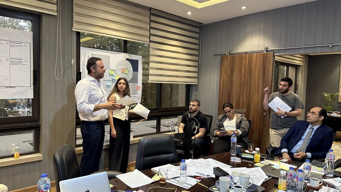 Two participants standing to present their group's work, sticky notes visible on the grid behind them