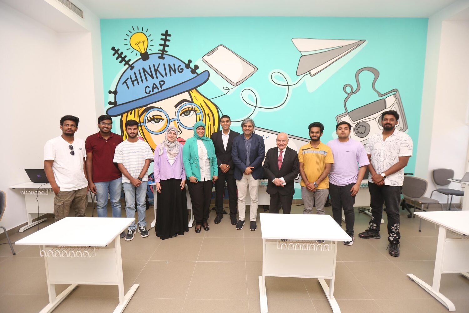 Group photograph in the computer lab, students and hosts lined up in front of a wall mural of a girl wearing a Thinking Cap.
