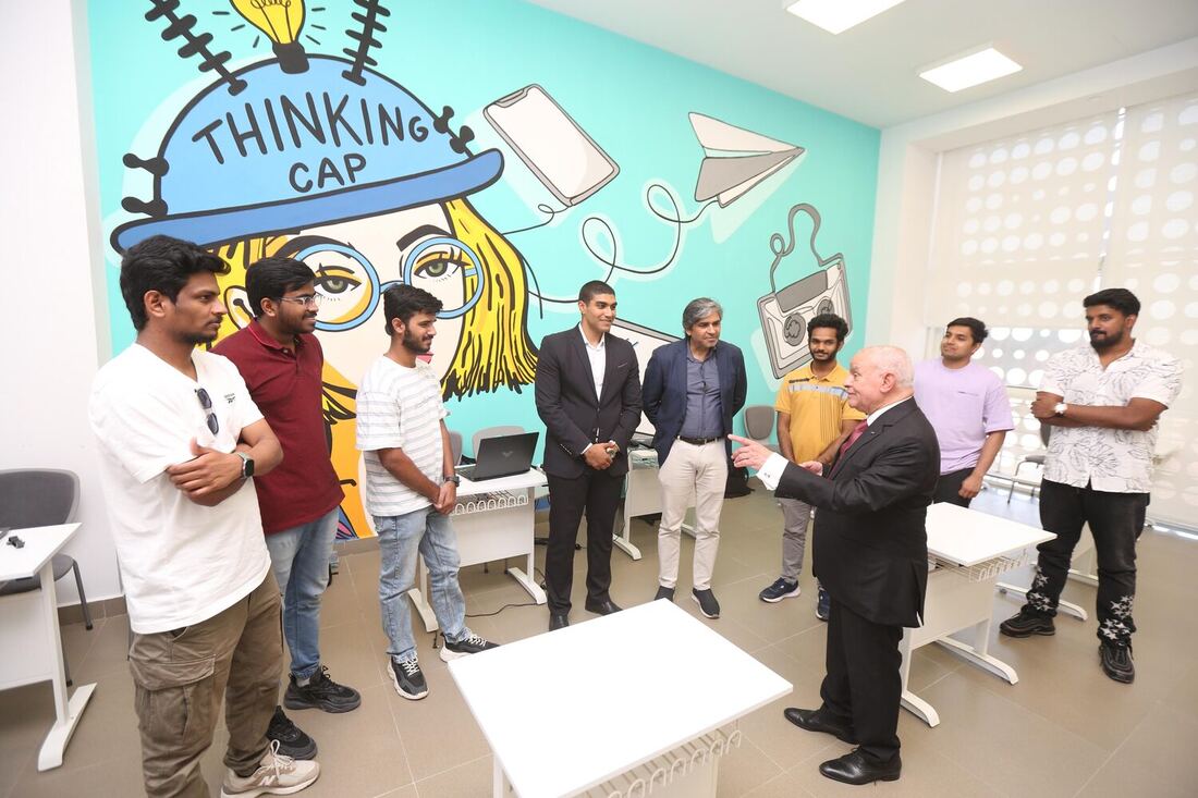 Students and visitors talking in the computer lab under the Thinking Cap mural, desks pushed aside.