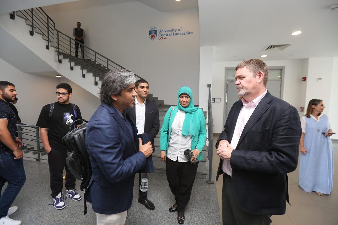 The campus atrium beneath a University of Central Lancashire sign, Tarry Singh in conversation with two hosts while students wait by the stairs.