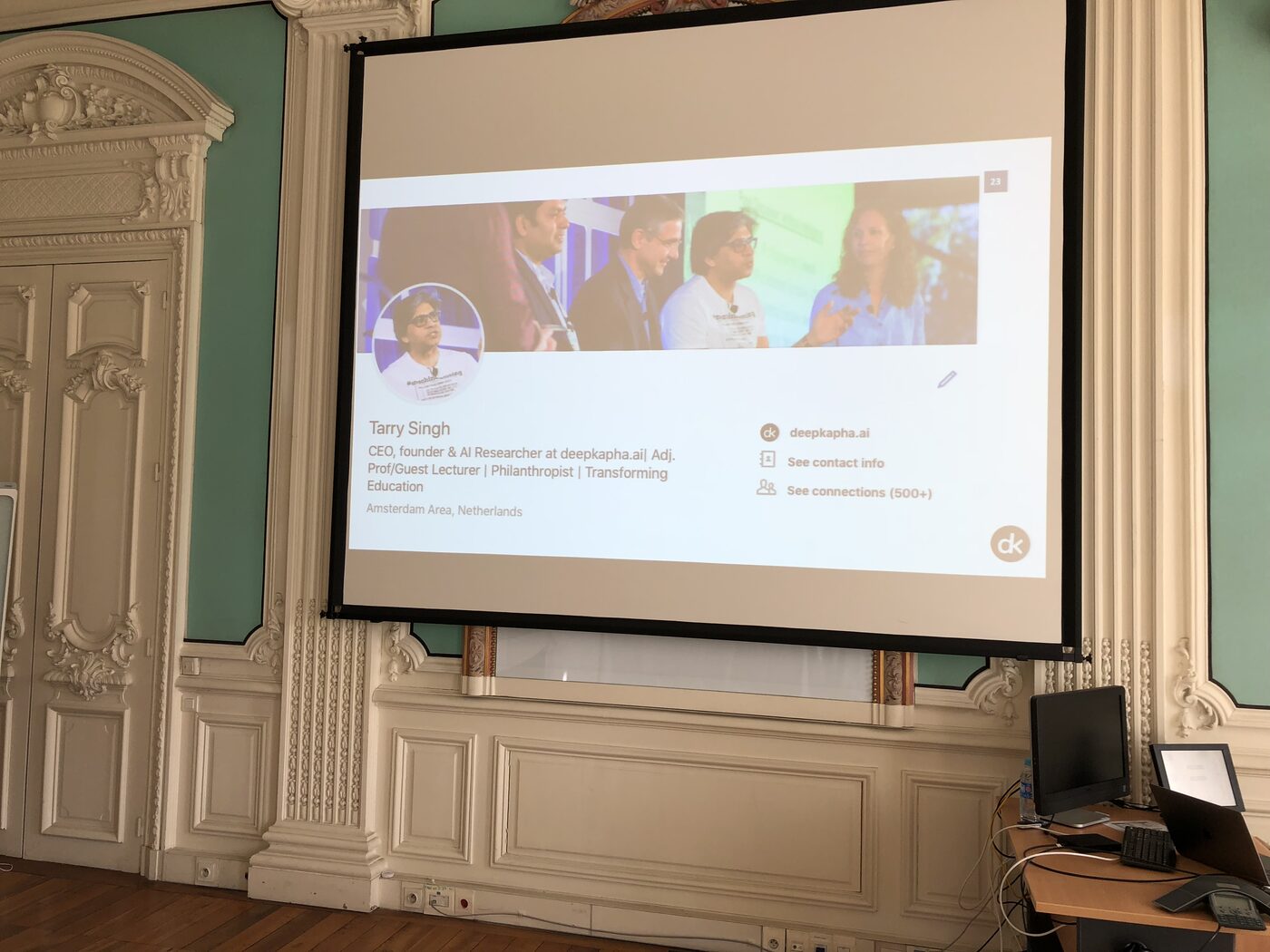 The projection screen in the presentation room at NAVER Labs Europe, showing the speaker introduction slide for Tarry Singh of deepkapha.ai.