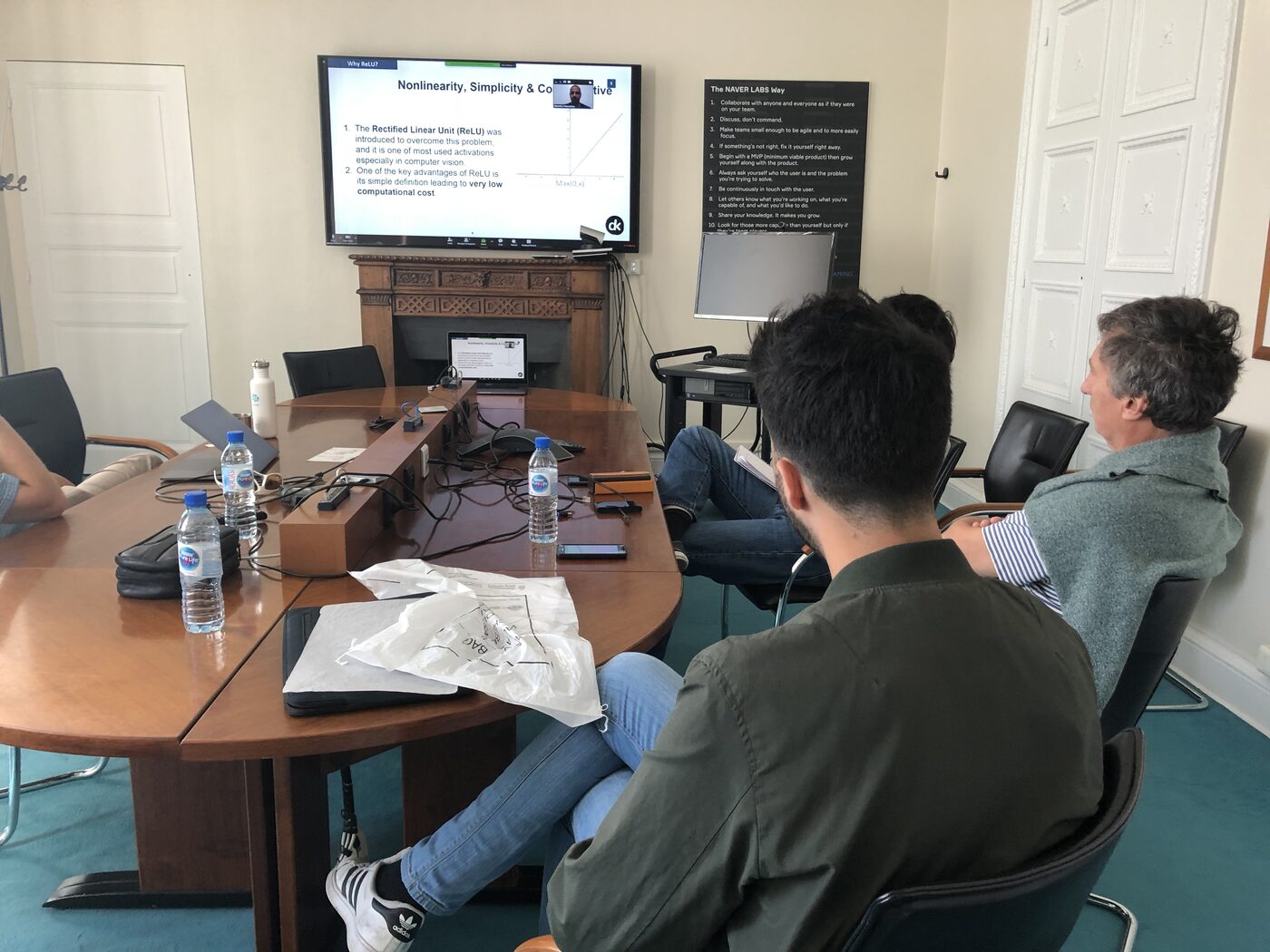 Two participants at the conference table watching the ReLU section of the deck on the wall screen.