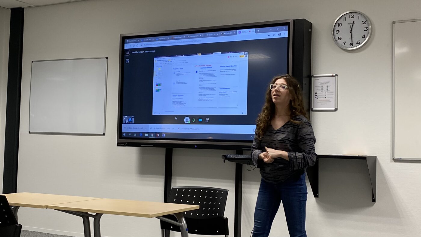 A student speaks to the room with a shared slide behind her, the presenter joining from elsewhere on the call.