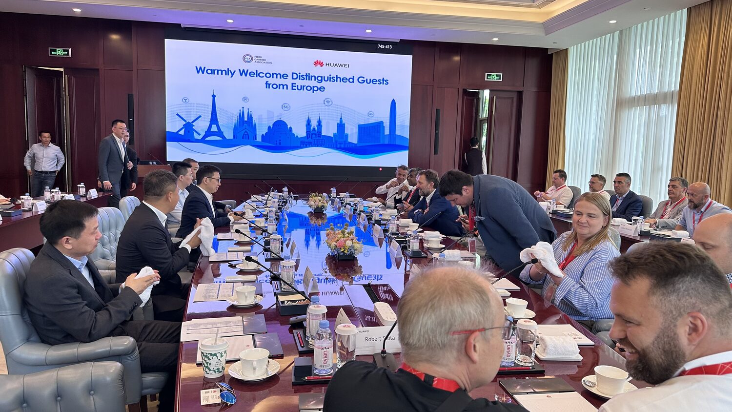 The European delegation and Huawei hosts seated around a boardroom table under the welcome screen, Shenzhen, 30 June early afternoon.