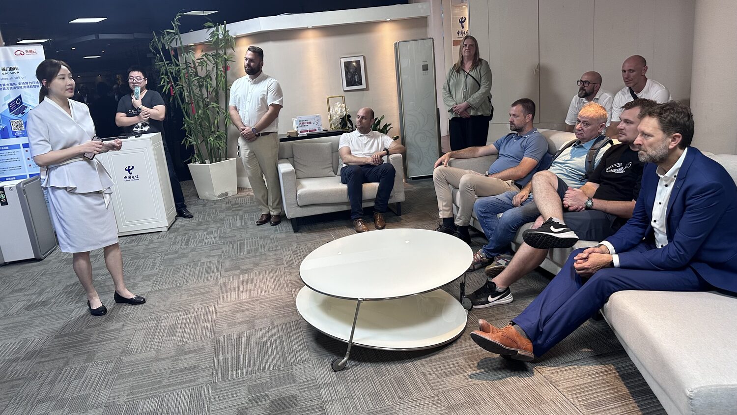 A China Telecom host briefs the standing and seated delegation in a retail space in Lujiazui, Shanghai, 3 July. China Telecom and Tianyi Cloud signage on the wall behind.