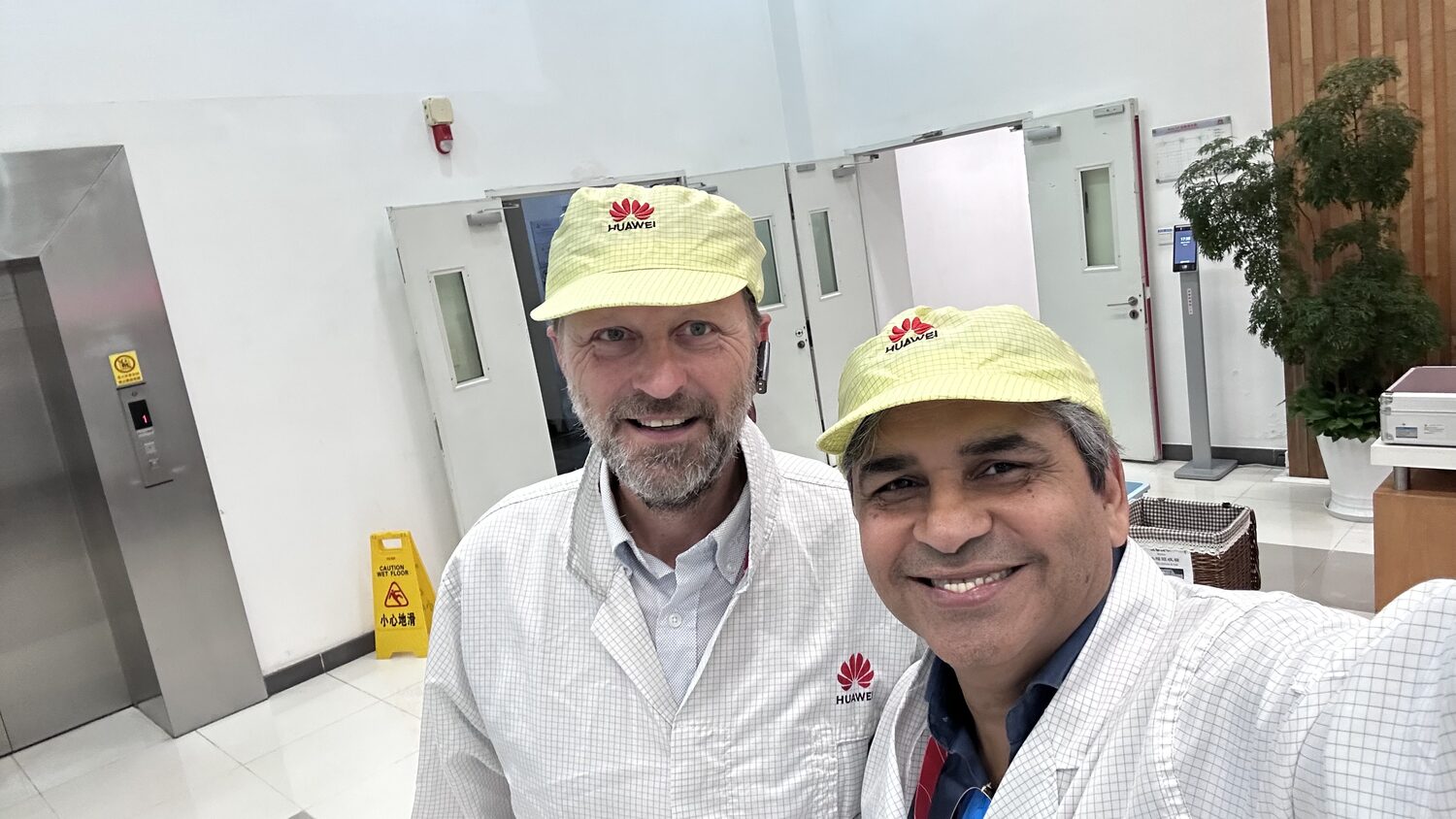 Two delegates in Huawei-issued white ESD coats and yellow Huawei caps at the entrance to a production area, Songshan Lake, Dongguan, 1 July.