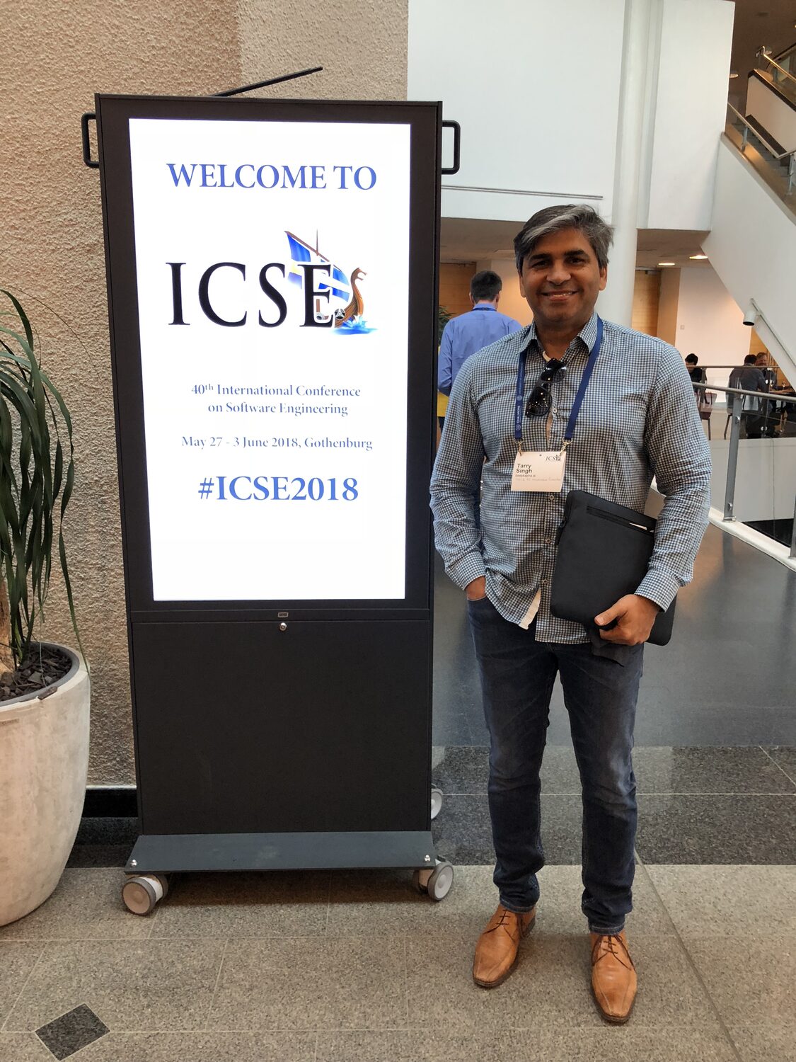 Tarry Singh beside the ICSE 2018 welcome sign in the venue atrium, badge on, folder under his arm.