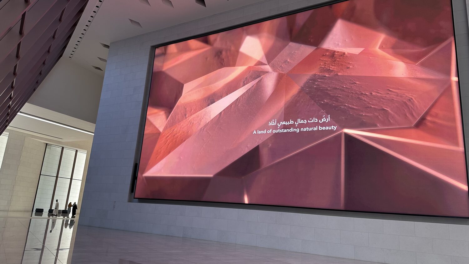 A wall screen in Muscat carrying a red three-dimensional subsurface visualisation, the faceted blocks of a reservoir model.