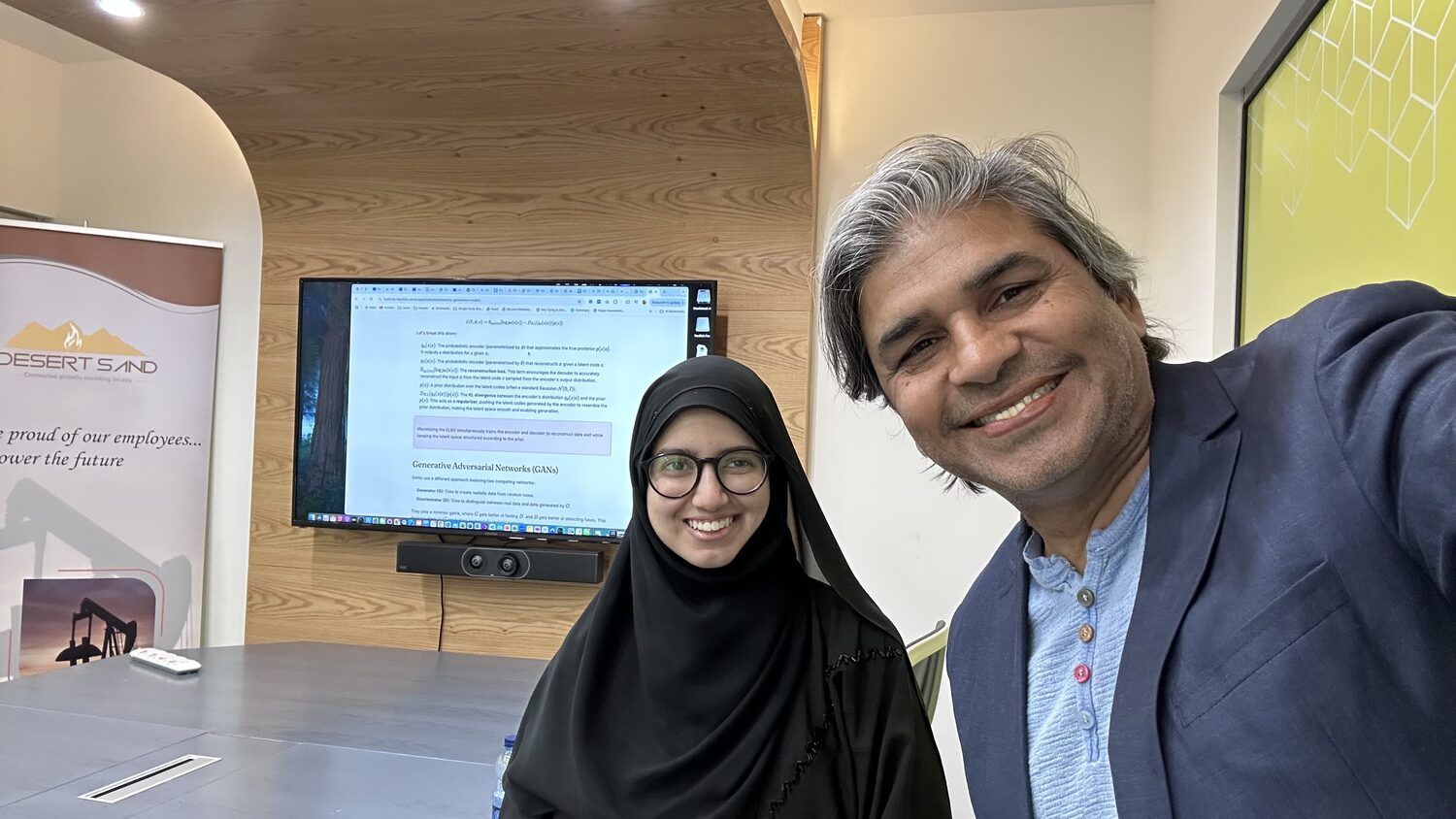 A working session in the Desert Sand Oil & Gas meeting room, the wall screen carrying the variational autoencoder slide.
