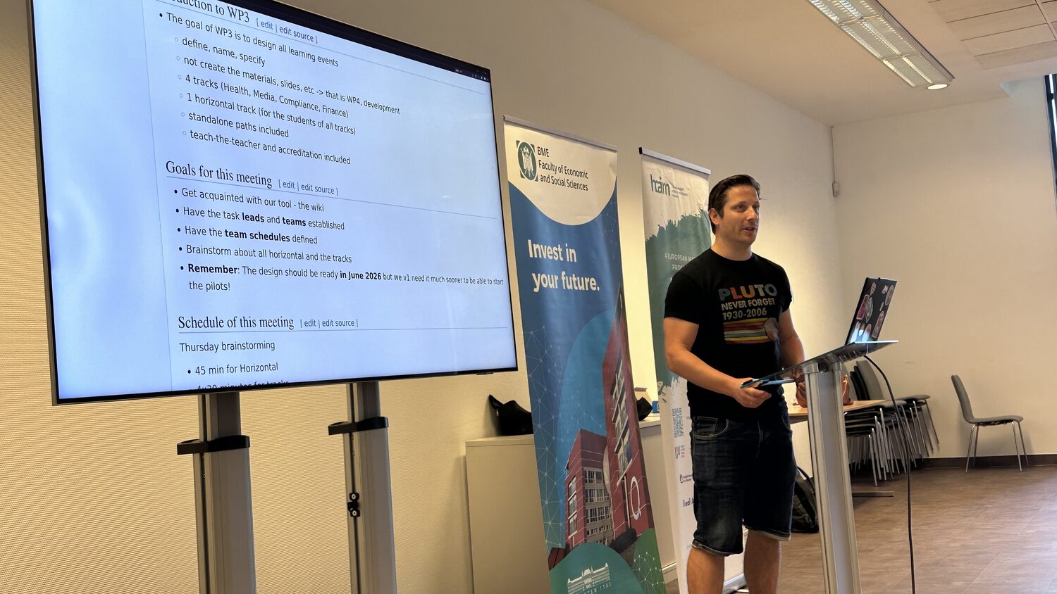 Mihály Héder of BME presenting the WP3 goals and process from the lectern, the wiki page listing the four tracks projected beside BME and HCAIM roll-up banners.