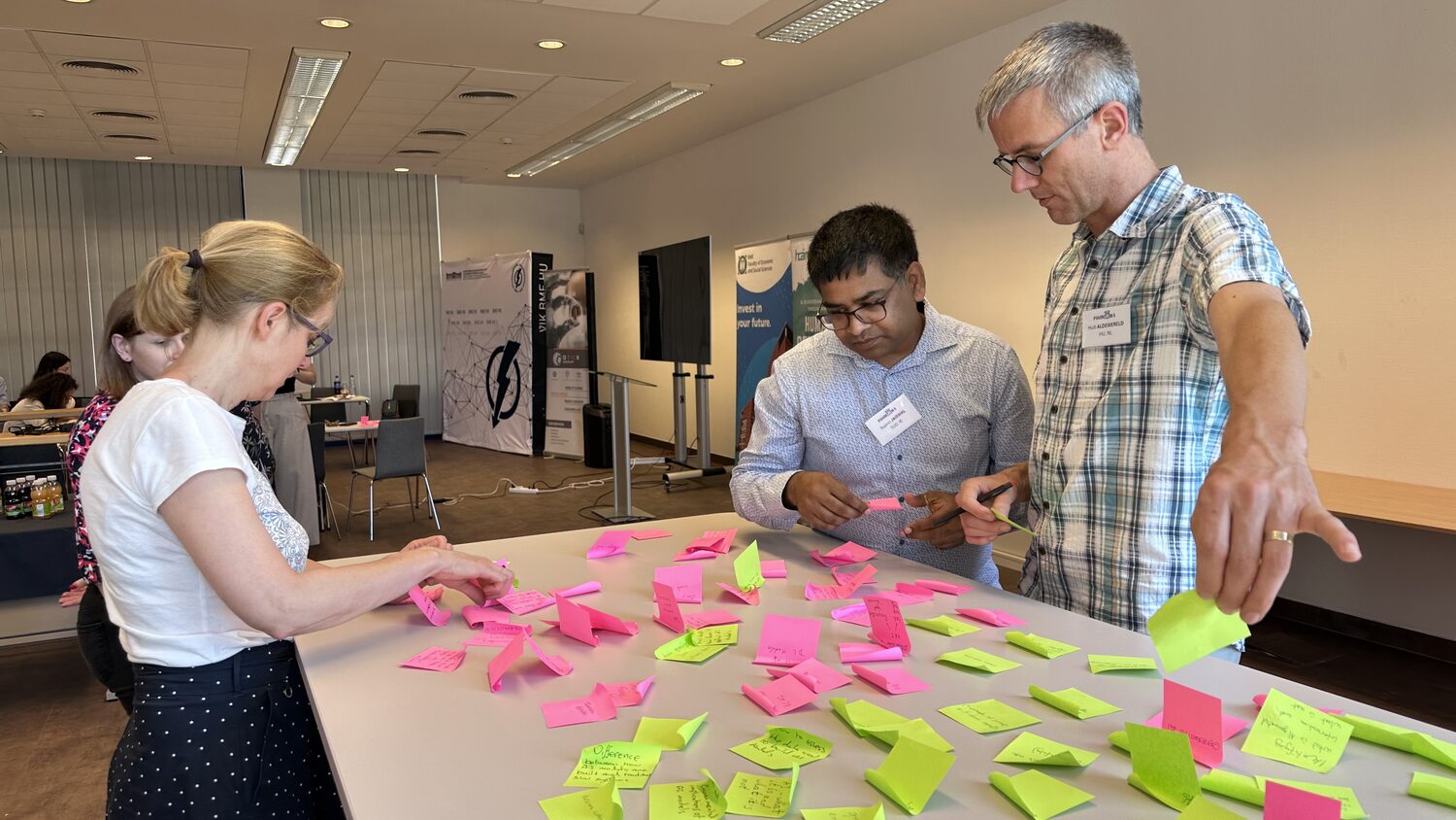 Three partners standing over a table covered in pink and green sticky notes during the brainstorming session.