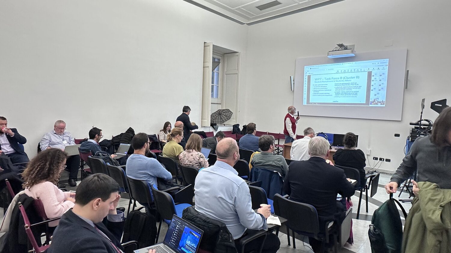 Wide view of the plenary, high ceiling and shuttered window, the WP7 slide on the projector screen.