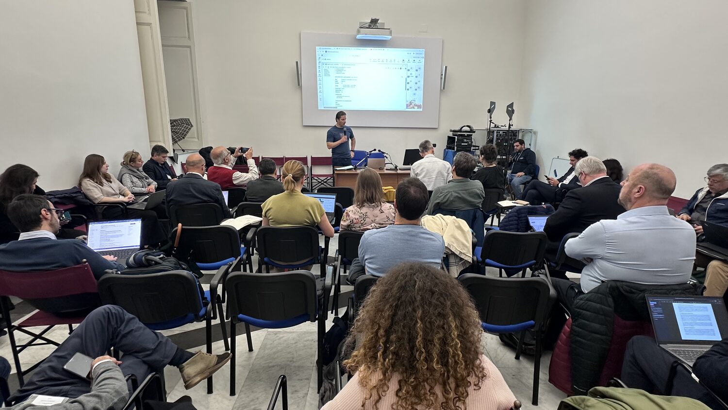 A second speaker at the screen with an administration form open, delegates and the camera position along the right-hand wall.