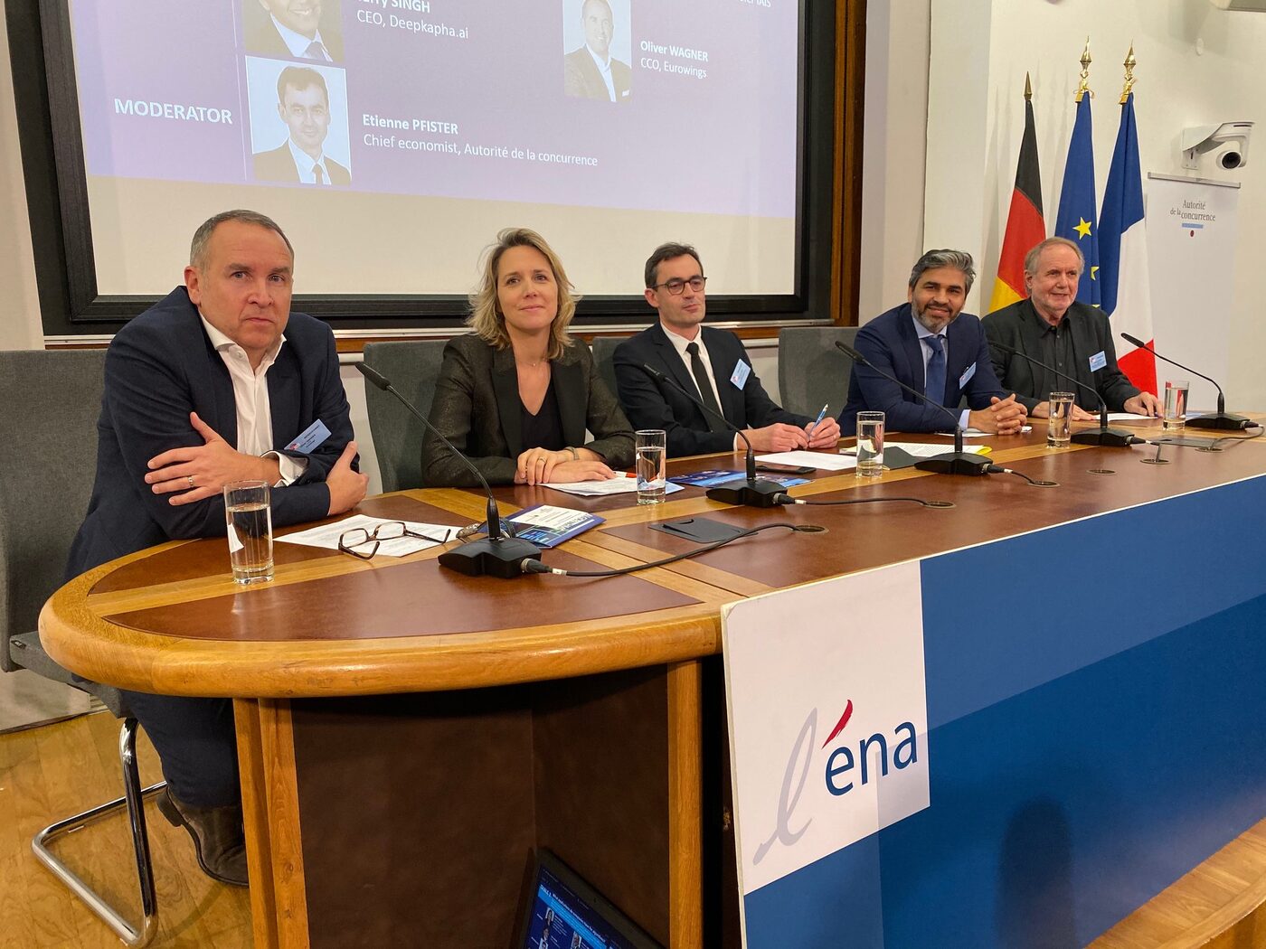 Five panellists seated behind the ENA conference table under a screen listing the speakers and moderator, with German, European and French flags to the right and an Autorité de la concurrence banner behind.