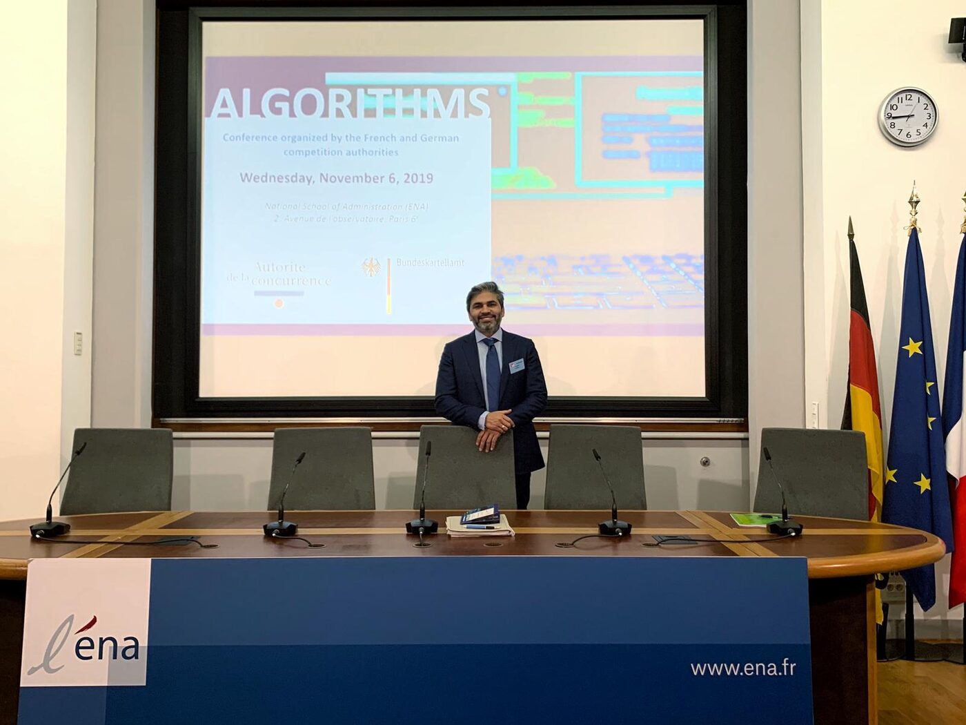 Tarry Singh standing behind the ENA panel table in front of the conference title slide, which gives the organisers, the date and the venue address.