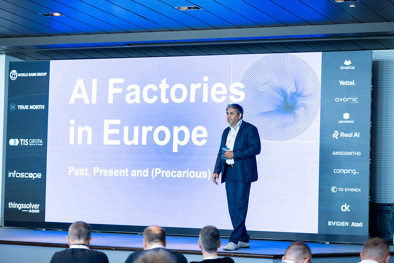 Tarry Singh on the AI Summit Adria stage beside a title slide reading AI Factories in Europe, delegates seated in the foreground.