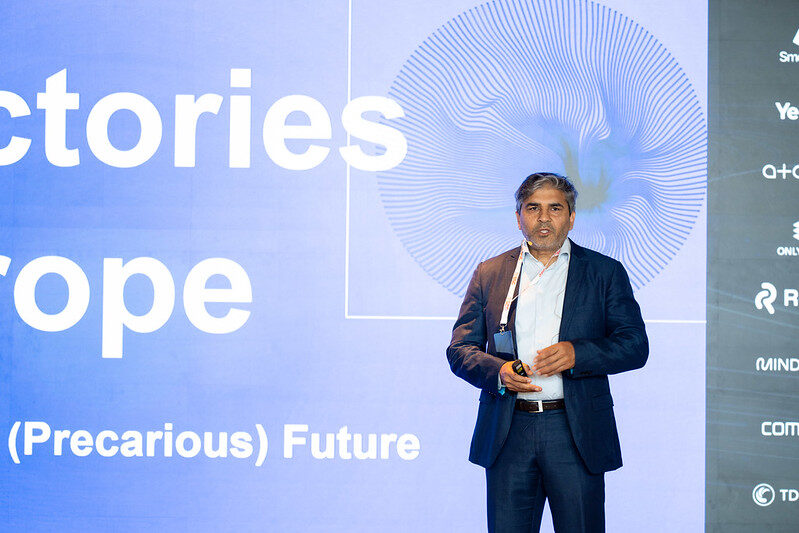 Tarry Singh on stage in front of the AI Factories in Europe title slide and the vertical rail of partner logos.