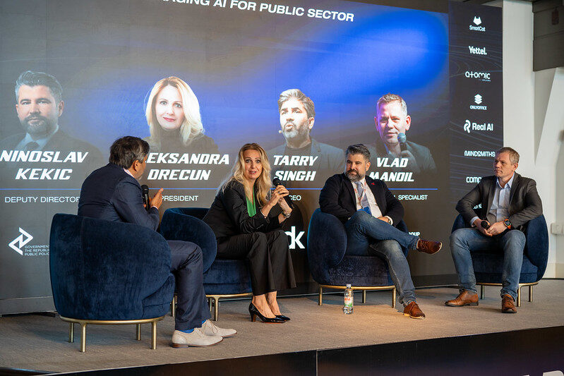 The public sector panel in conversation, four speakers seated with their names and roles on the screen behind.