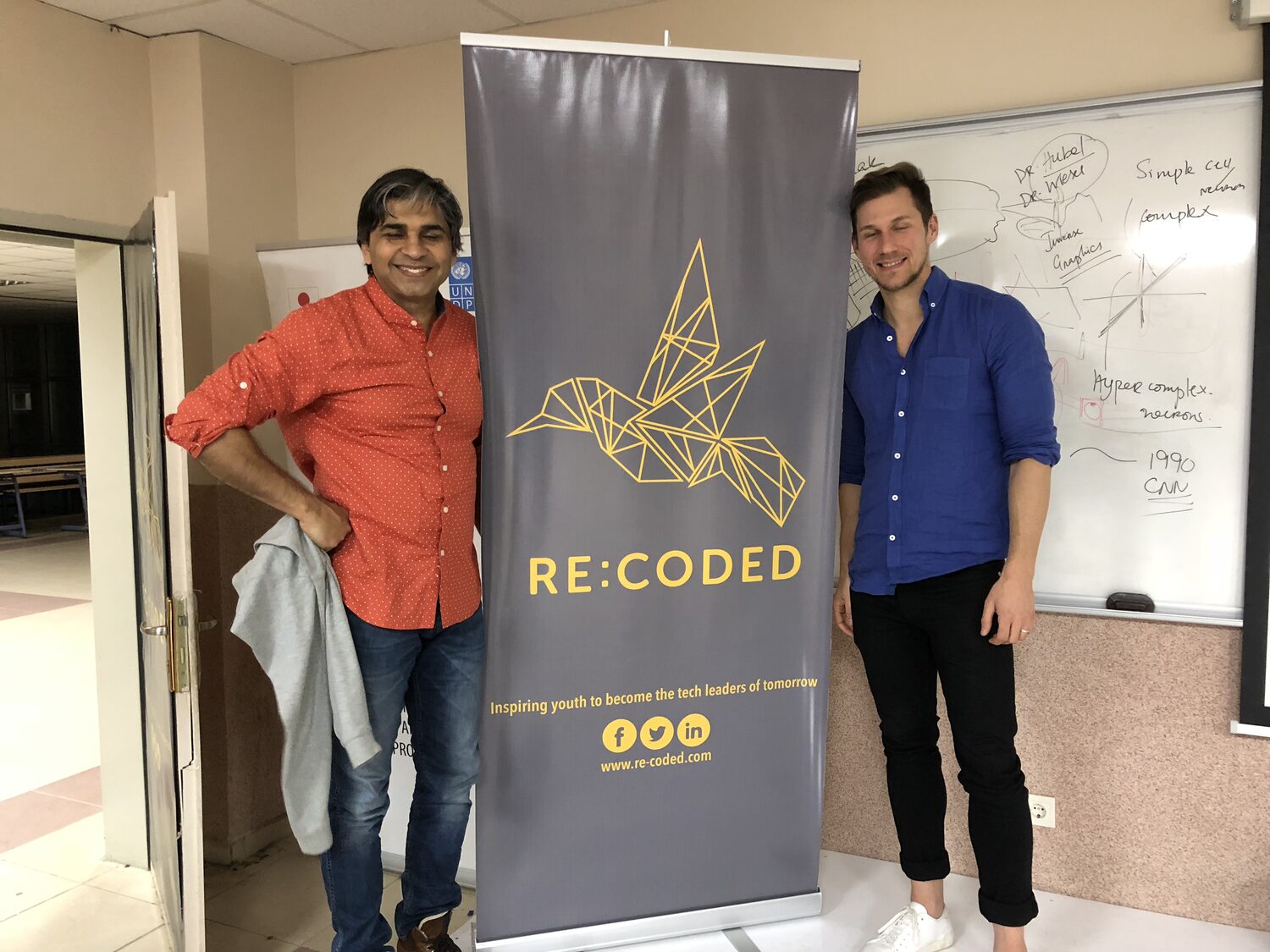 Tarry Singh and a Re:coded host either side of the Re:coded roll-up banner, the teaching whiteboard behind them tracing Hubel and Wiesel through to convolutional networks