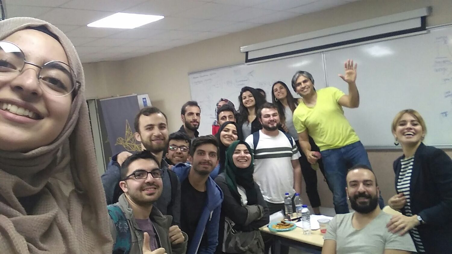 A second cohort photograph from the same session, taken by a participant, the group gathered in front of the whiteboard
