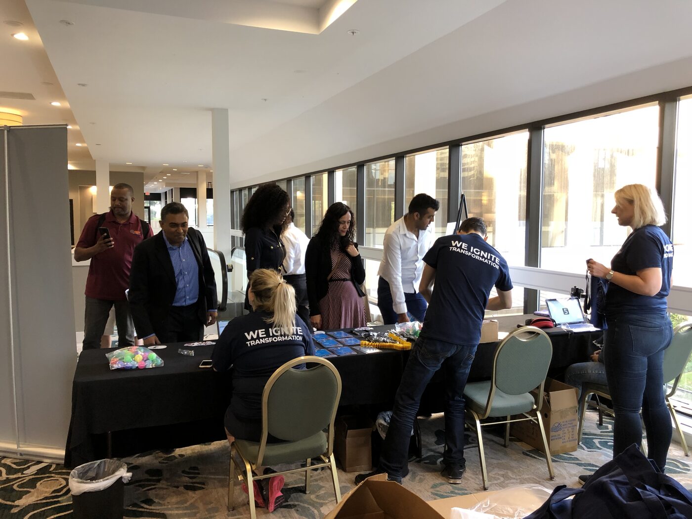 The DataScienceGO expo and registration floor beside a glass atrium, event crew in navy shirts reading WE IGNITE TRANSFORMATION working the tables.