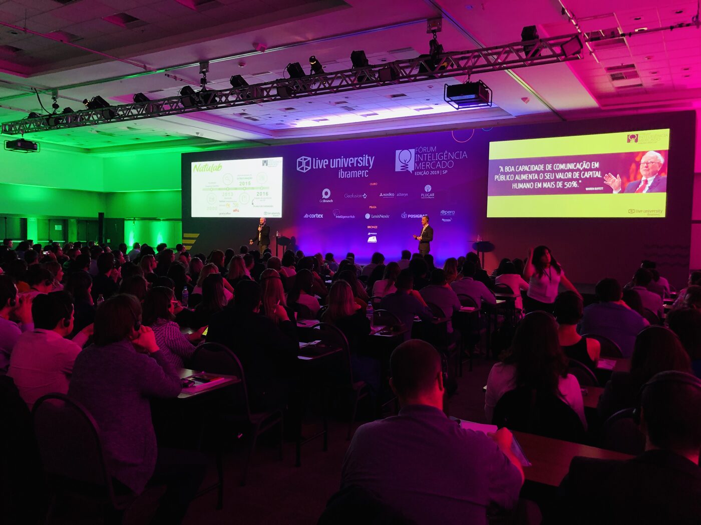 The main ballroom at Fórum Inteligência Mercado 2019 in São Paulo on 10 June, seen from the back of a full room, with two speakers on stage and the Live University Ibramerc sponsor wall behind them.
