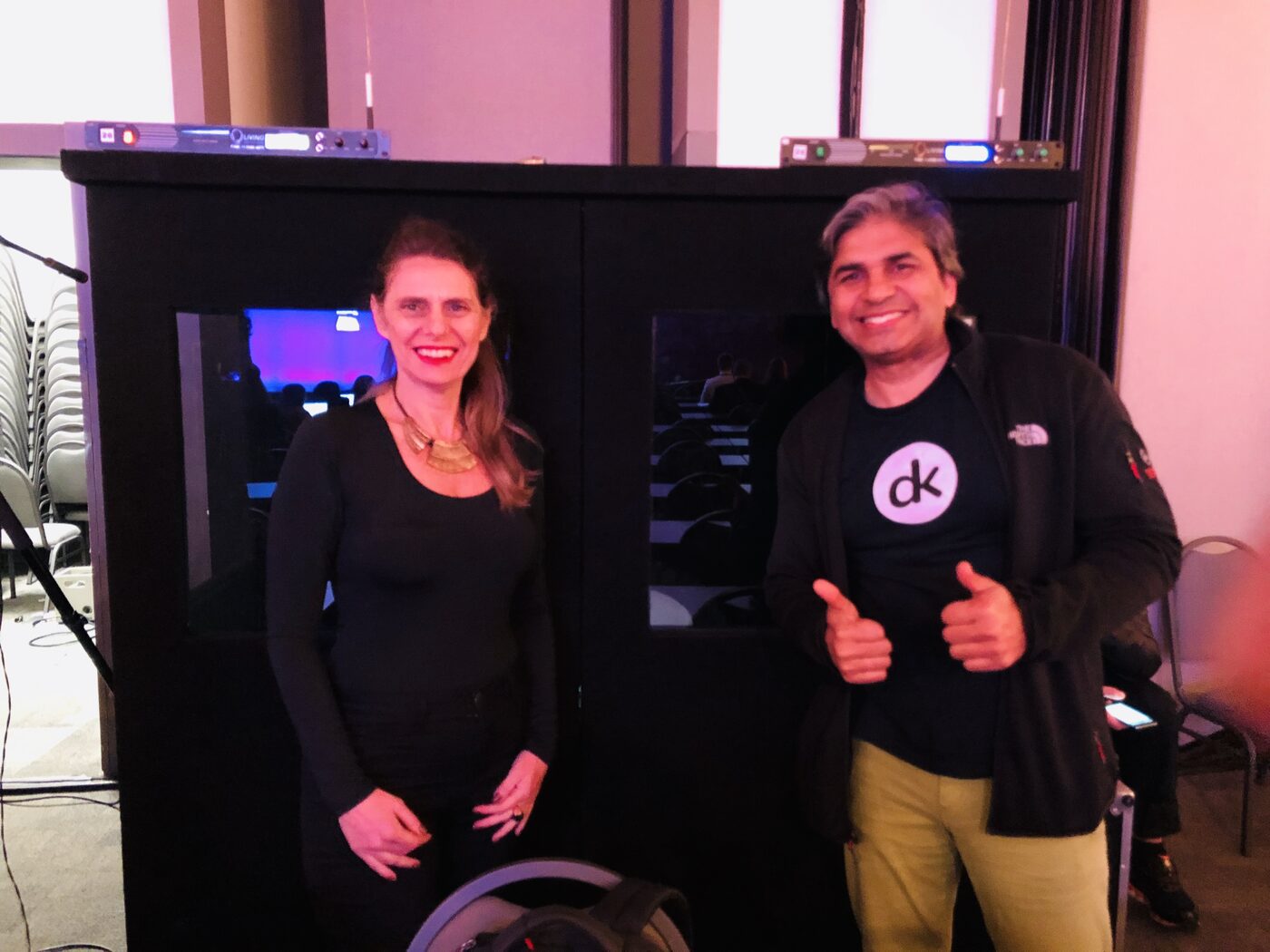 Tarry Singh, in a deepkapha.ai shirt, standing with another attendee at the simultaneous interpretation booths on the morning of 11 June, the darkened auditorium visible through the booth windows.