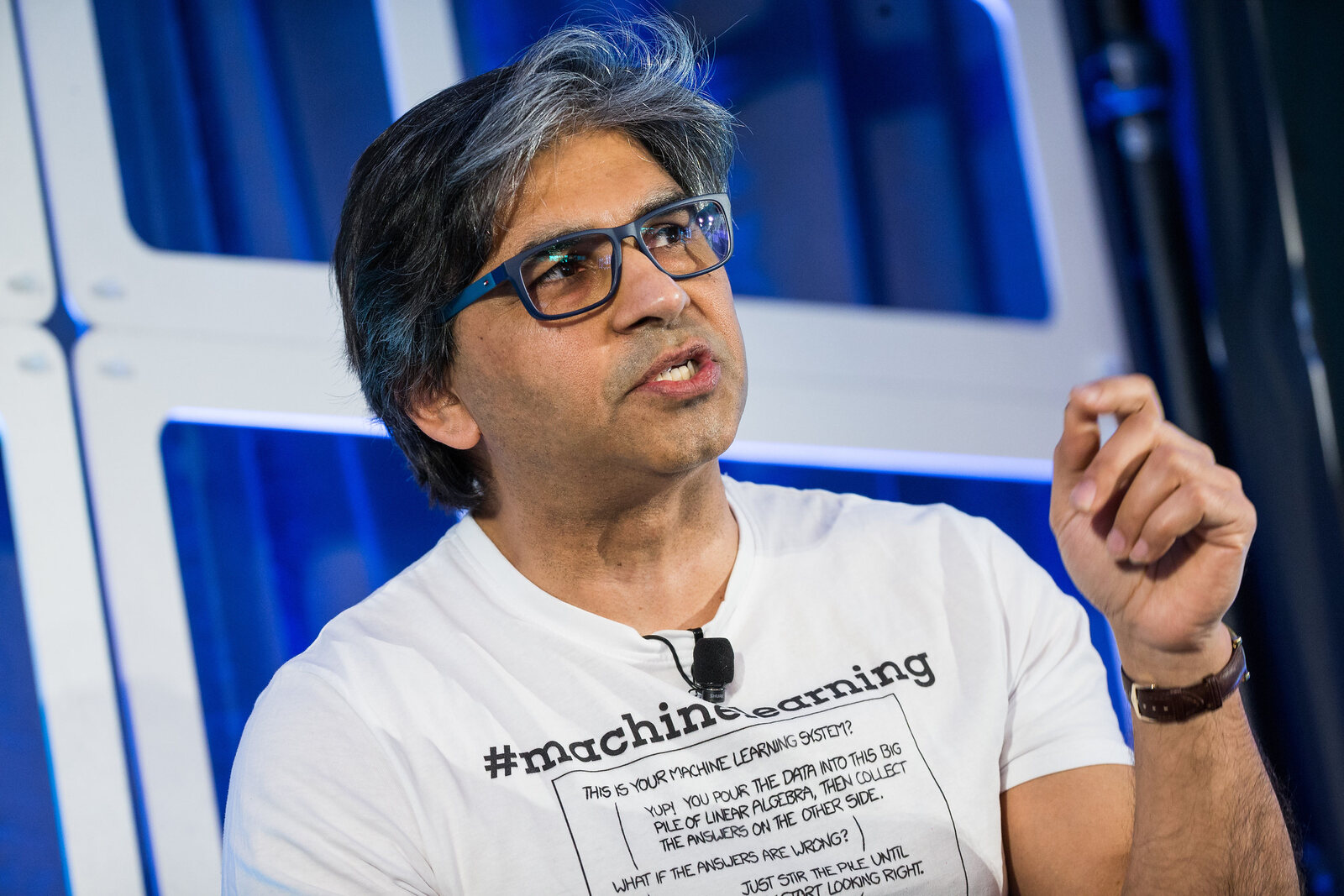 Tarry Singh mid-sentence on the panel, hand raised to make a point, wearing the #machinelearning T-shirt.